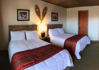 Updated guest room with two double beds, striped orange and red bed throws over crisp, white comforters,  Black and white photos of area and vintage snowshoes hang over beds